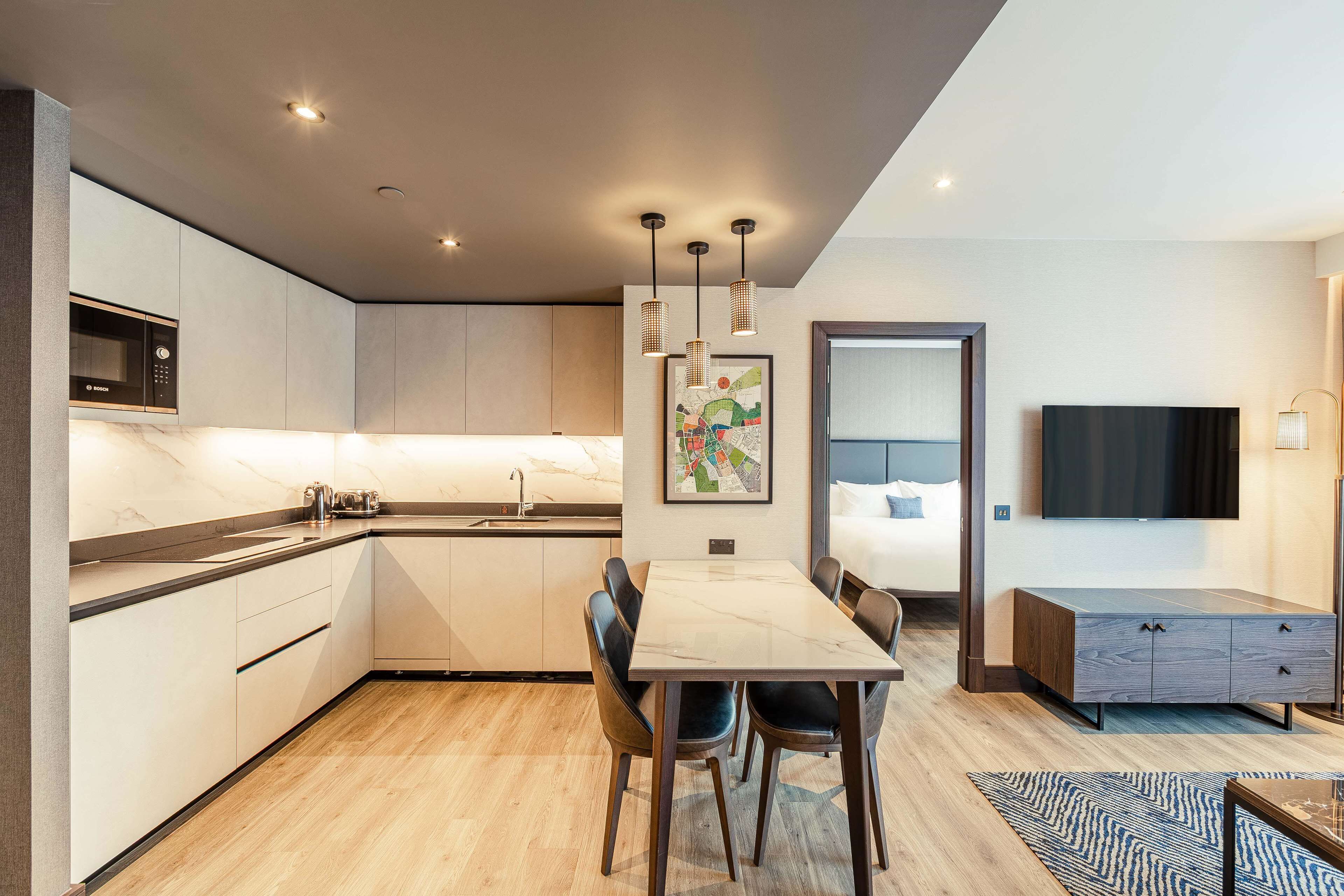 Una cocina moderna con microondas integrado, una zona de comedor con una mesa y sillas de mármol, y un salón con televisor y sofá.