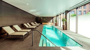 A modern indoor swimming pool with lounge chairs and potted plants. - The Fellows House Cambridge, Curio Collection by Hilton (Cambridge)
