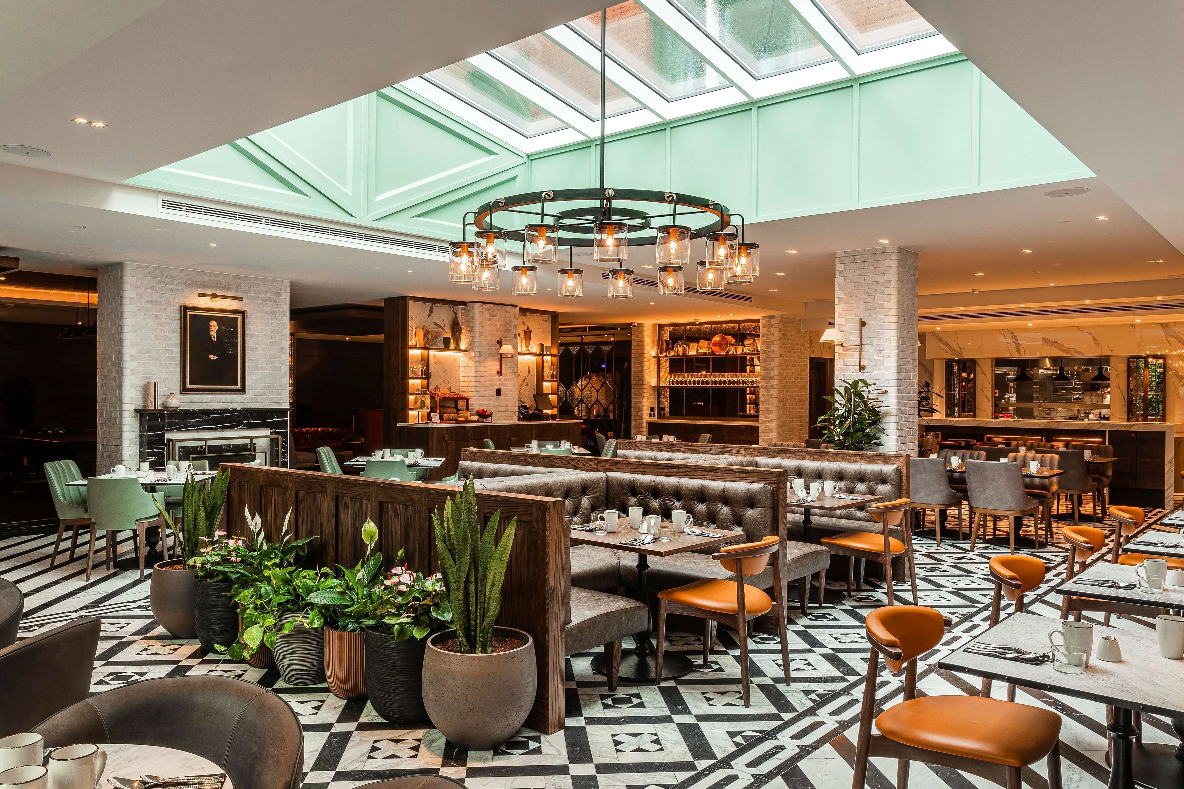 Un restaurante moderno con techos altos, un candelabro central y una variedad de opciones de asientos, incluyendo cabinas y mesas.