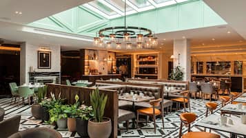 Un restaurante moderno con techos altos, un candelabro central y una variedad de opciones de asientos, incluyendo cabinas y mesas.