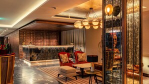 A modern lobby with a marble reception desk, red armchairs, a round table, and a large mirror. - The Fellows House Cambridge, Curio Collection by Hilton (Cambridge)