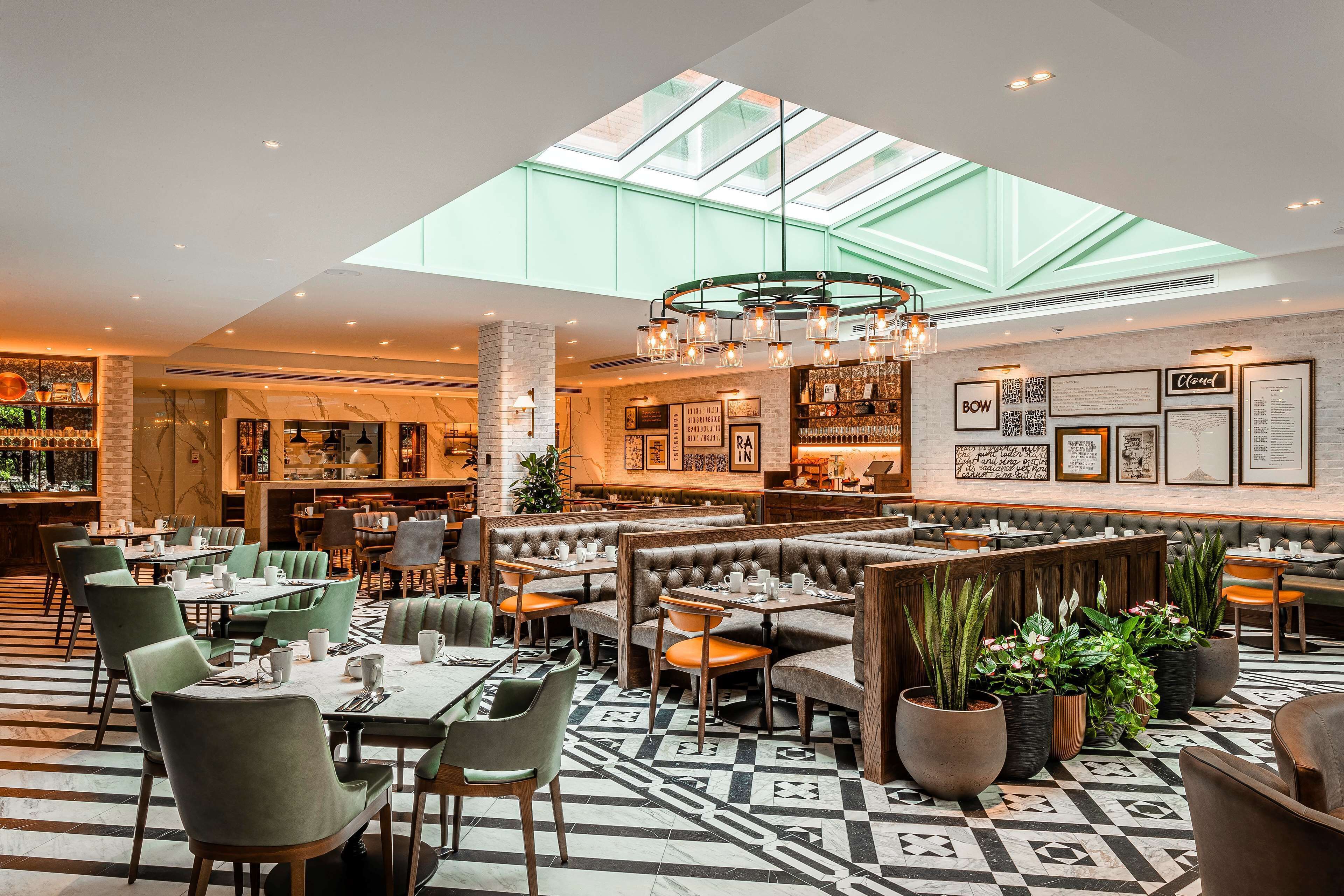 Een ruim restaurant met hoge plafonds, een dakraam en diverse zitmogelijkheden, zoals hoekbanken en tafels.