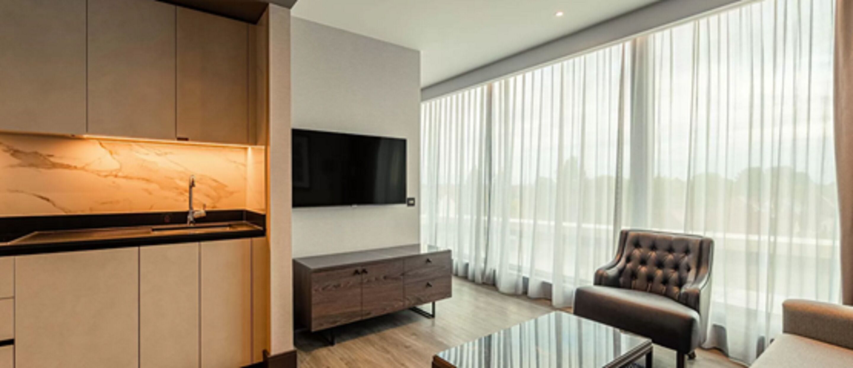 Una sala de estar moderna con una mesa de centro de vidrio, un sillón de cuero y un televisor de pantalla plana montado en la pared.