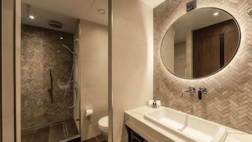 Een moderne badkamer met een wand in herringbone-patroon, een grote spiegel en een inloopdouche.