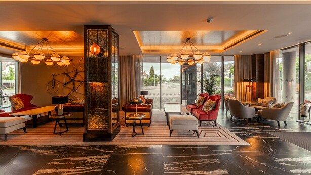 A modern hotel lobby with a large glass wall, a central column, and multiple seating areas. - The Fellows House Cambridge, Curio Collection by Hilton (Cambridge)