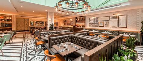 Un restaurante moderno con techos altos, un candelabro central y una combinación de asientos tipo cabina y mesas.
