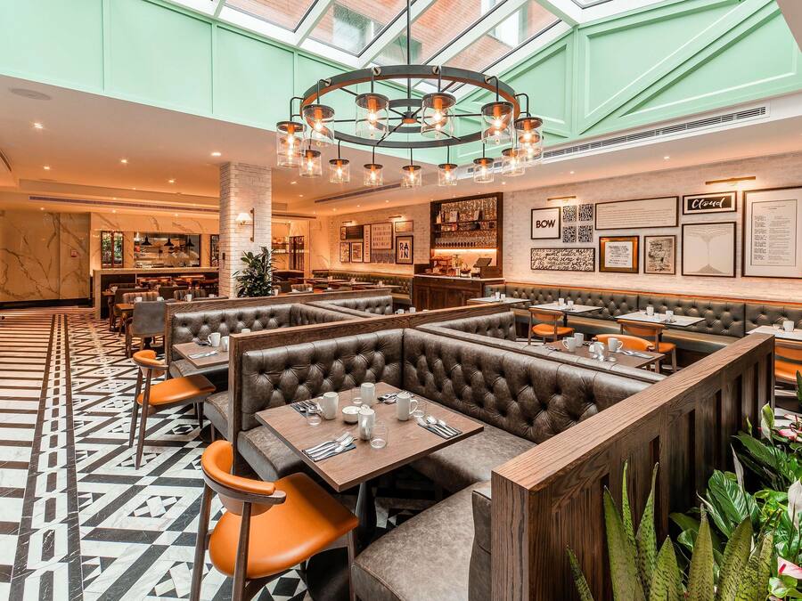Un restaurante moderno con techos altos, un candelabro central y una combinación de asientos tipo cabina y mesas.