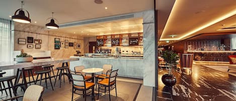 A modern bar area with a marble countertop, multiple seating options including bar stools and chairs, and a variety of bottles and glasses on display.