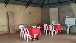Un vaste espace intérieur doté d’un sol carrelé et de tables recouvertes de nappes rouges, entourées de chaises en plastique blanches.