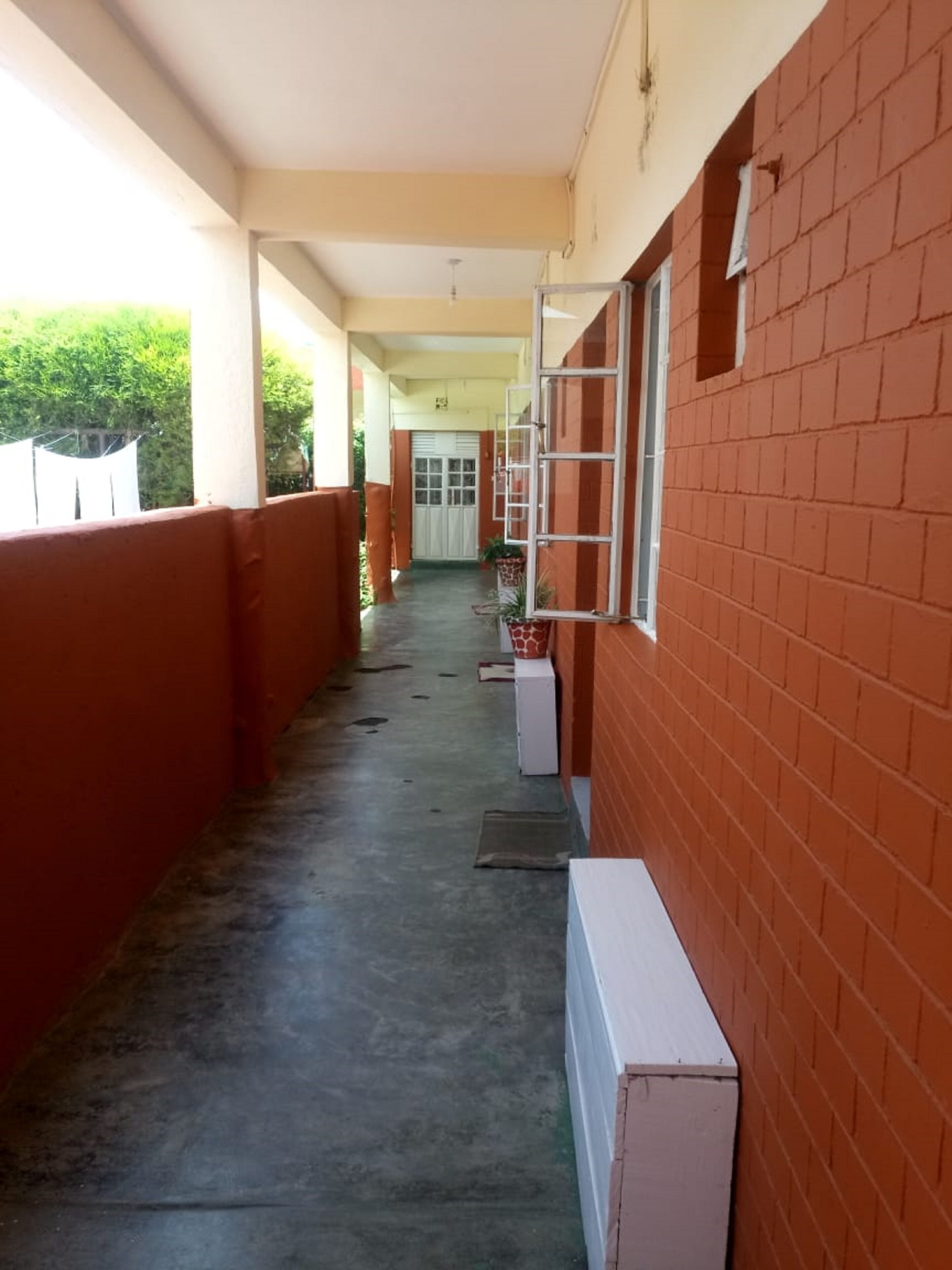 A corridor with a red brick wall, a white door at the end, and a window with a metal frame.