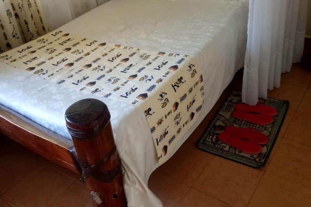 A bed with a patterned bedspread, white curtains, and a wooden headboard.