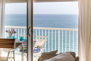 A balcony with a view of the ocean, a table with chairs, and a window with curtains.