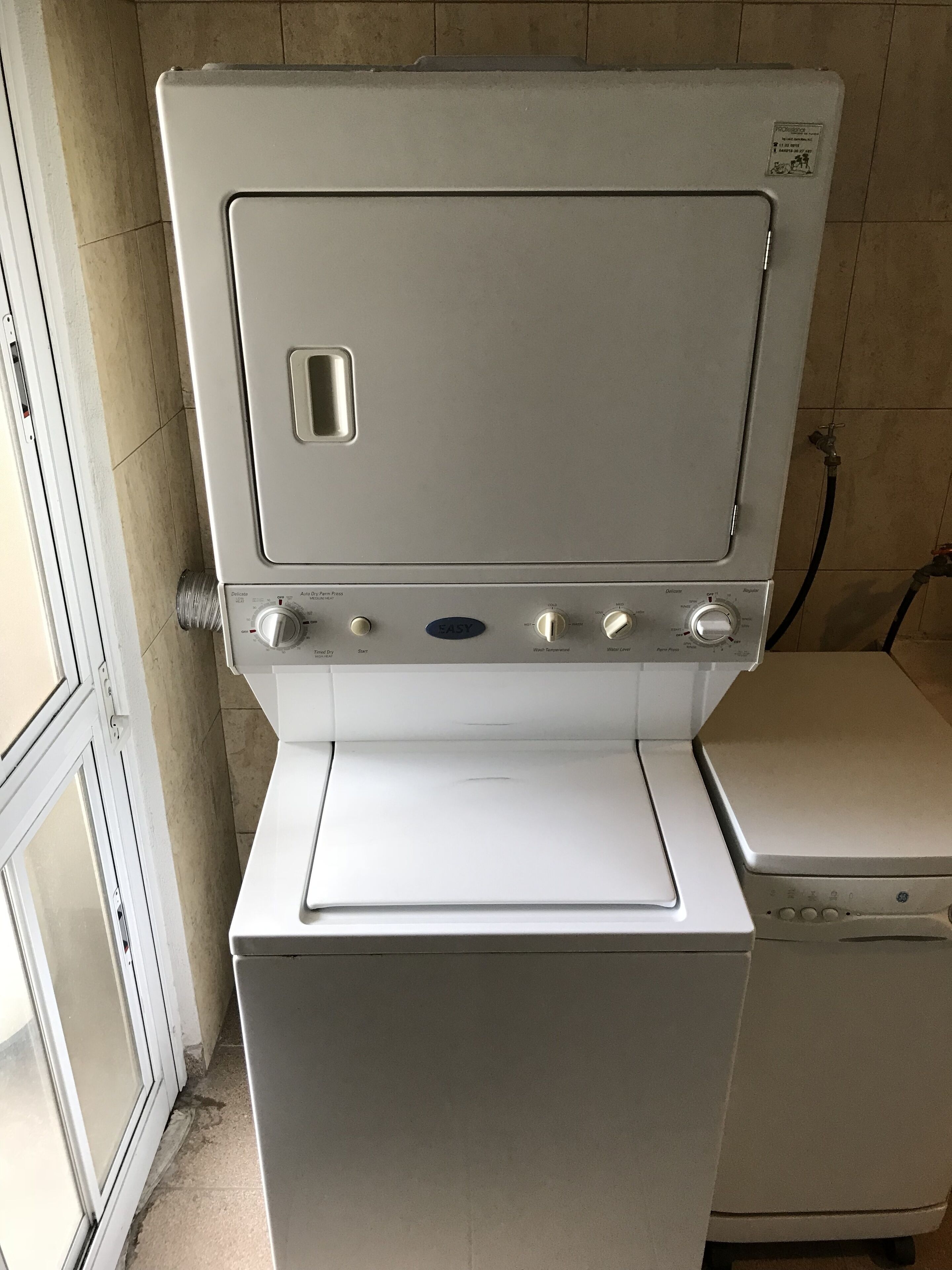 Une petite buanderie blanche, équipée d’un lave-linge à chargement frontal et d’un sèche-linge.