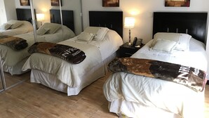 Habitación de hotel con dos camas, cada una con ropa de cama blanca y una manta marrón. Mesitas de noche con lámparas y teléfono. La habitación tiene un espejo grande y arte abstracto en las paredes.
