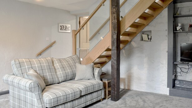 A living room with a plaid sofa, a wooden staircase, and a bookshelf with decorative items. - 2 bedroom accommodation in Melmerby, near Penrith (Melmerby, near Penrith)