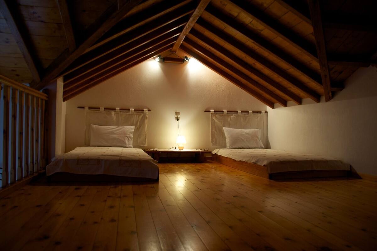 A small, cozy attic bedroom with two single beds, wooden beams, and a sloped ceiling.