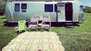 A vintage camper van parked in a grassy field with a small house in the background. - Airstream at The Goat (San Marcos)