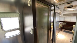 A compact RV interior with a kitchenette, a small dining area, and a sleeping space. - Airstream at The Goat (San Marcos)