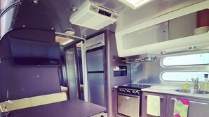A compact kitchen with a stove, sink, and a small countertop. - Airstream at The Goat (San Marcos)