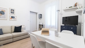A modern living room with a sofa, a dining table with chairs, a TV, and a bookshelf.