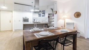 A modern kitchen with white cabinets, a wooden dining table set for four, and a dining area with a lamp and a hat on the wall. - Italianway - Savona 26 B (Milan)