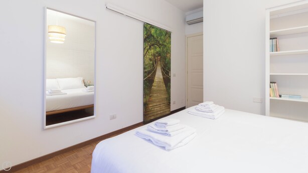A hotel room with a bed, a mirror, a painting of a bridge, a bookshelf, and a door. - Italianway - Savona 26 B (Milan)