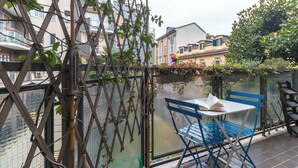 A balcony with a blue chair and a table, a bamboo trellis, and a view of buildings. - Italianway - Savona 26 B (Milan)