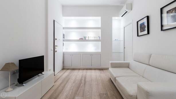 A modern, minimalist living room with a flat-screen TV, a white sofa, and a built-in bookshelf. - Italianway - Corso Genova 27 A (Milan)