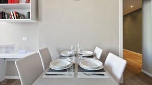 A dining area with a table set for four, white chairs, and a bookshelf with books. - Italianway - Largo Allegri 4 (Milan)
