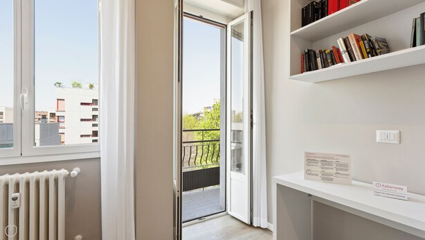 A modern apartment with a balcony, a white radiator, and a bookshelf filled with books. - Italianway - Largo Allegri 4 (Milan)