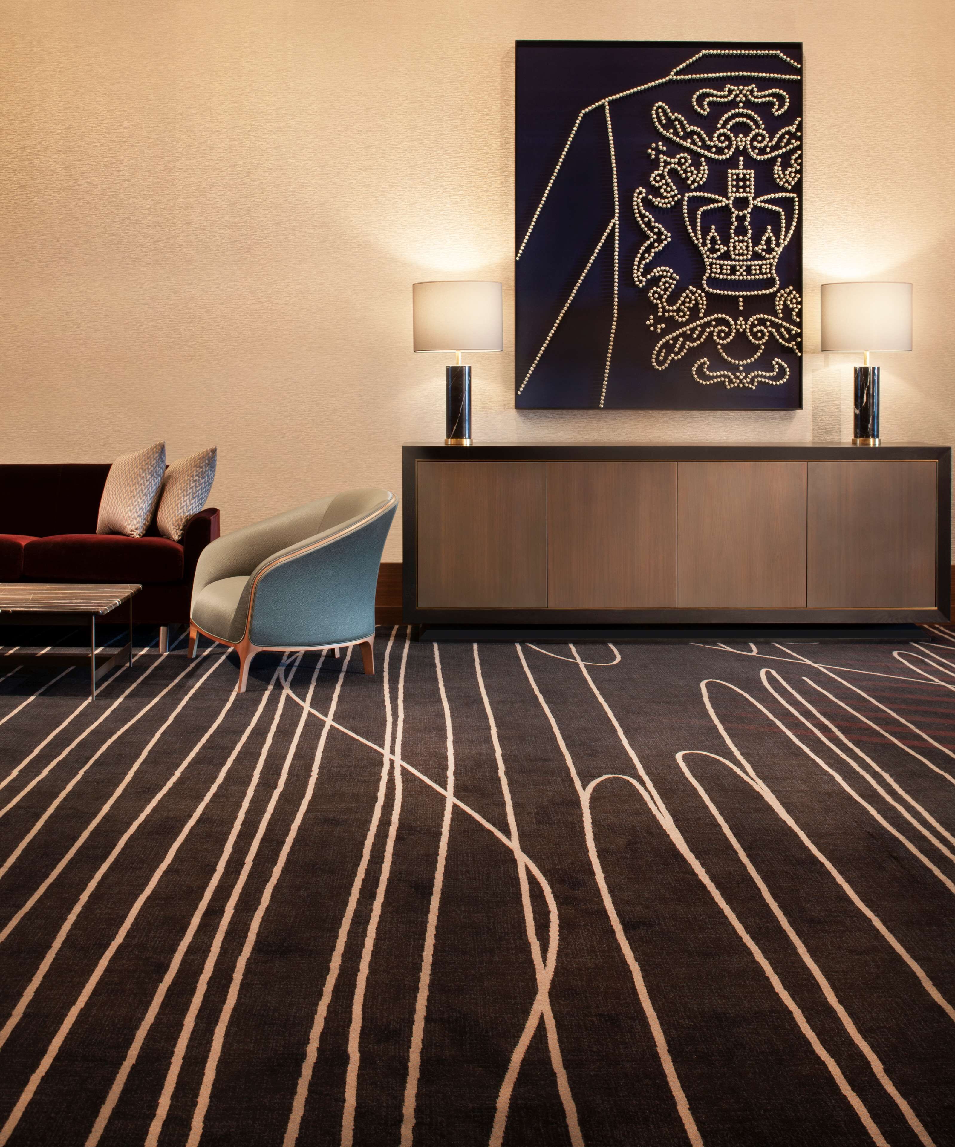 Vestíbulo de hotel con alfombra de diseño oscuro, un sillón azul, un sofá rojo y una obra de arte colgada en la pared.