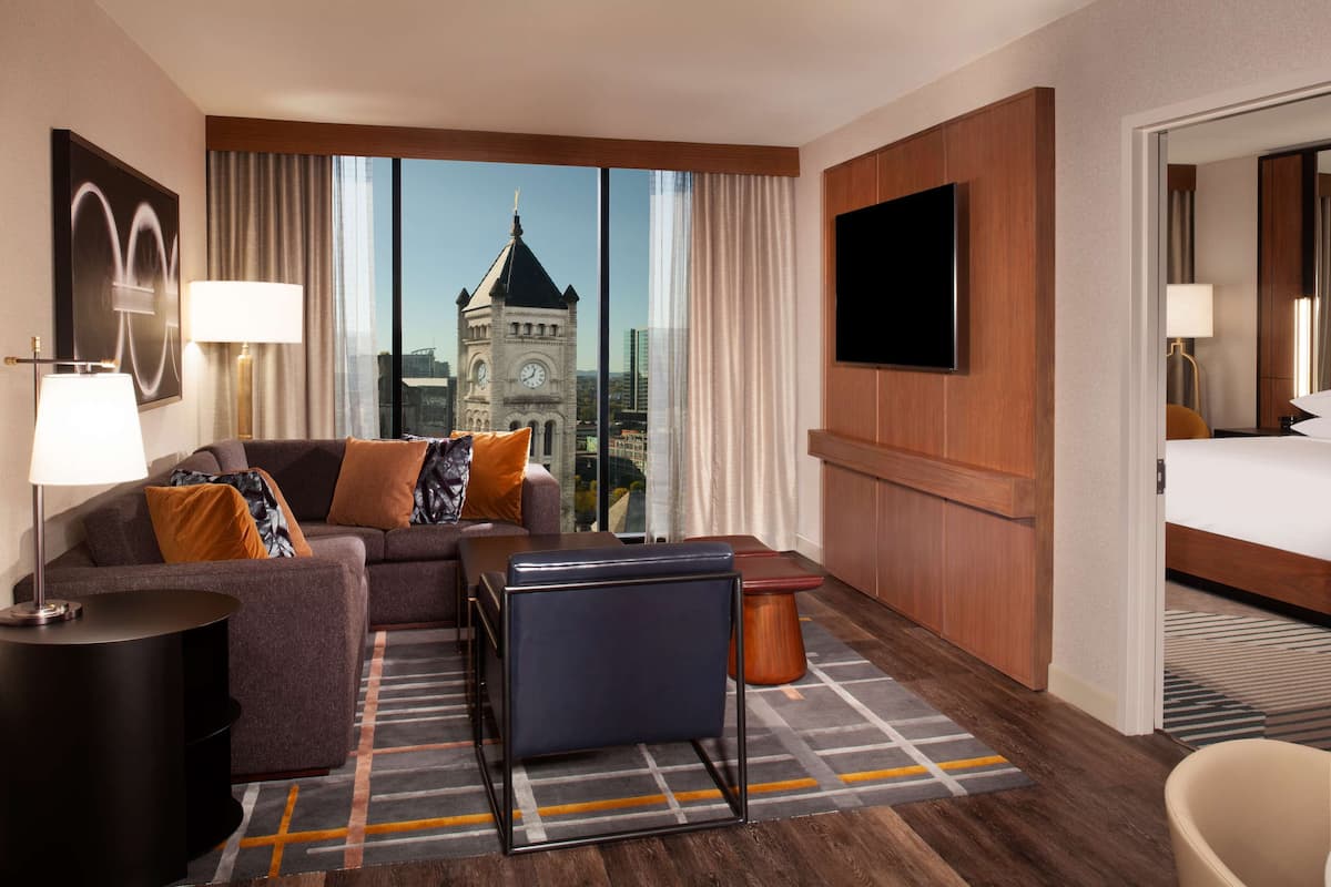 Een hotelkamer met een groot raam, een bank, een televisie, een bed en een bureau.