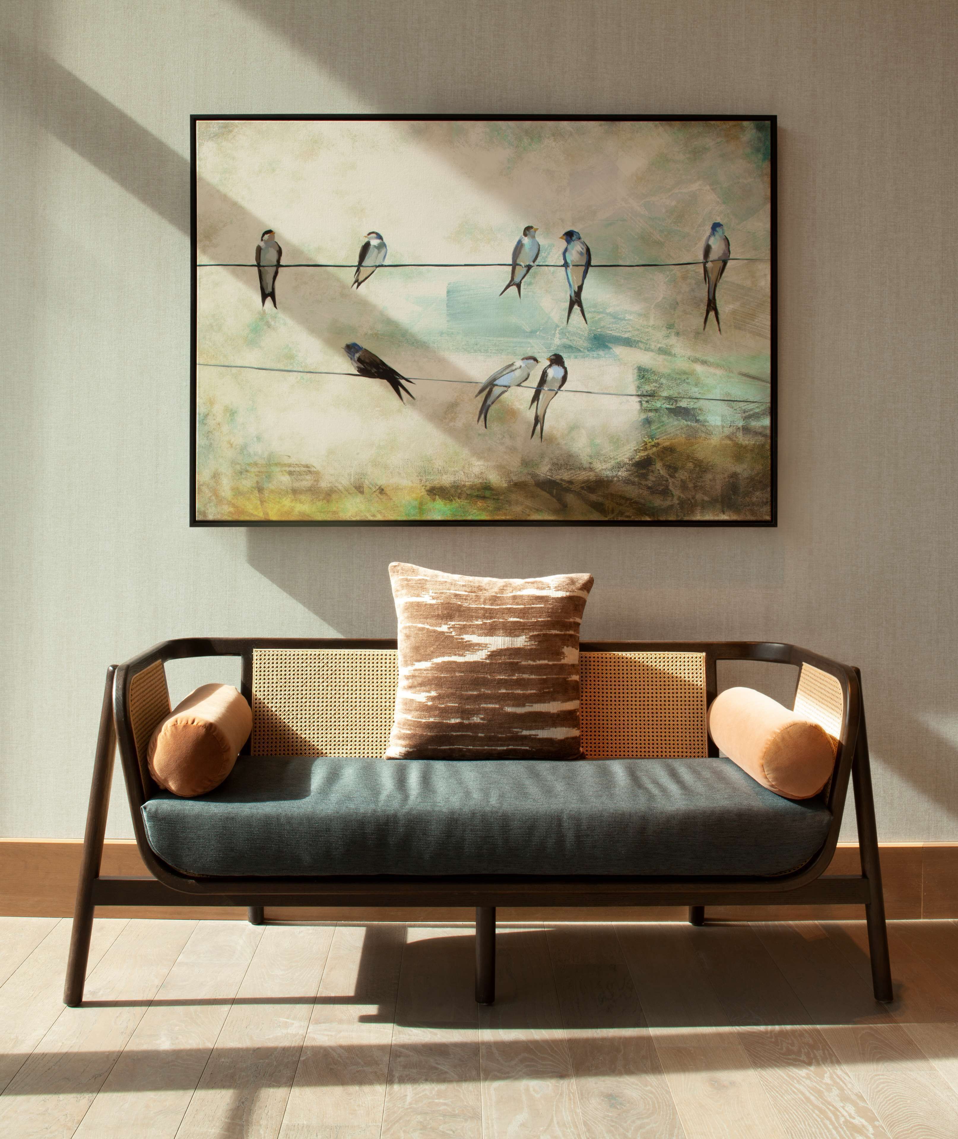 Ein modernes Sofa mit gewebtem Rücken und Kissen, vor einem Wandbild mit Vögeln auf einem Draht.