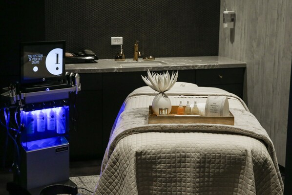 A hotel room with a bed, a bedside table, a small desk with a computer, and a wall-mounted TV.