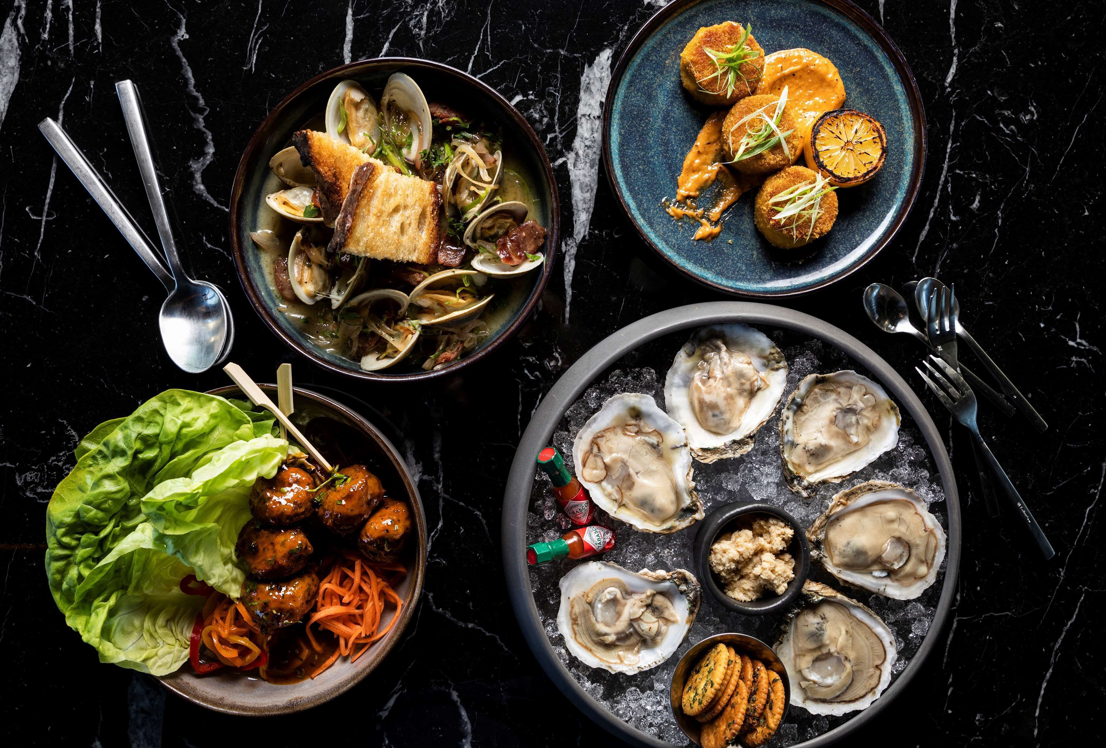 A variety of dishes including seafood, meatballs, and oysters on a marble table.