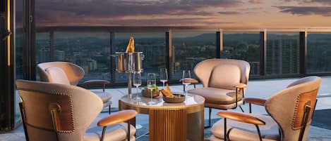 A rooftop terrace with a round table, four chairs, a wine glass, a bottle, and a view of the cityscape and moon.