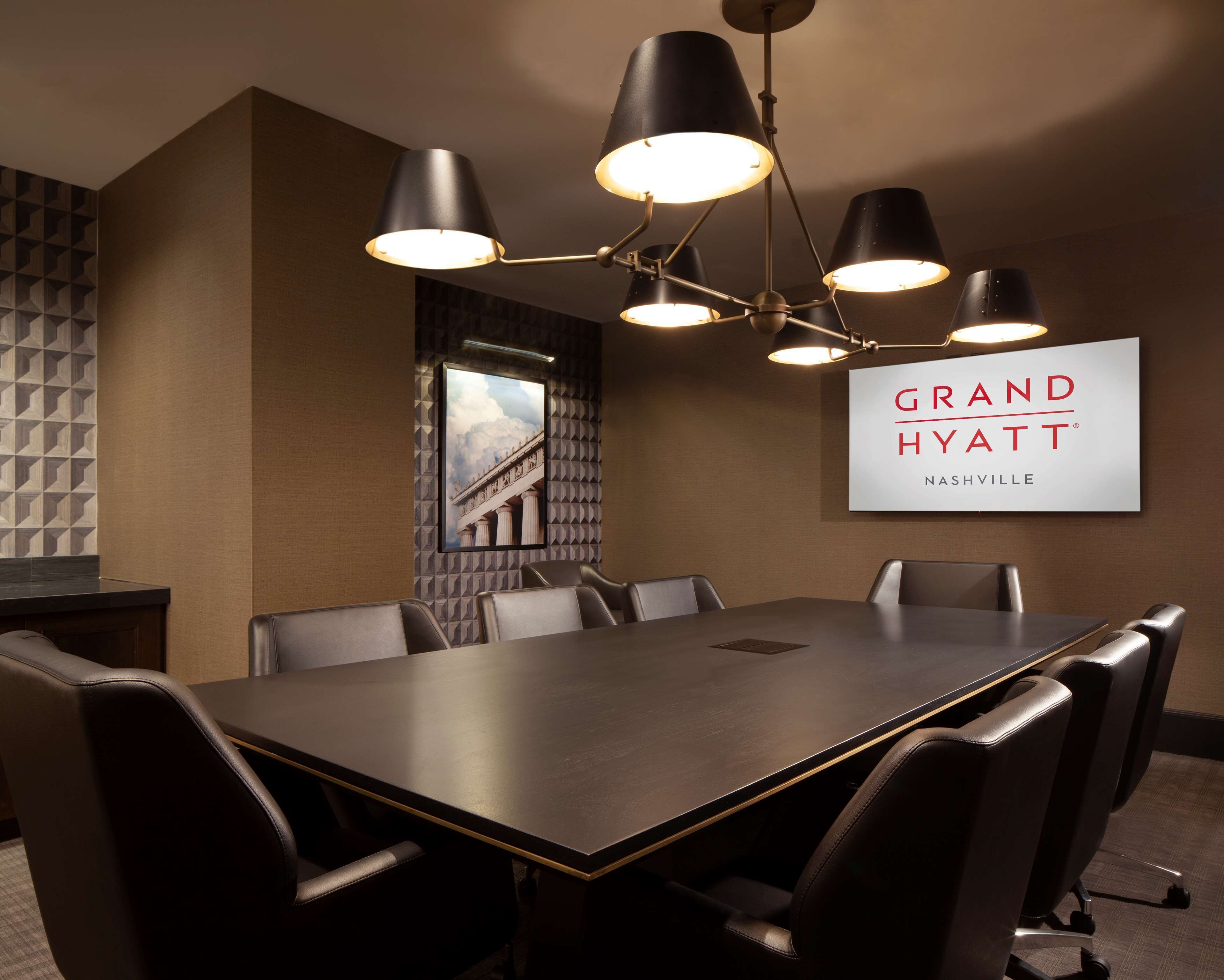 Ein Konferenzraum mit einem langen Tisch, mehreren Stühlen und einer Kandelaber. Ein Schild an der Wand trägt die Aufschrift 'Grand Hyatt Nashville'.