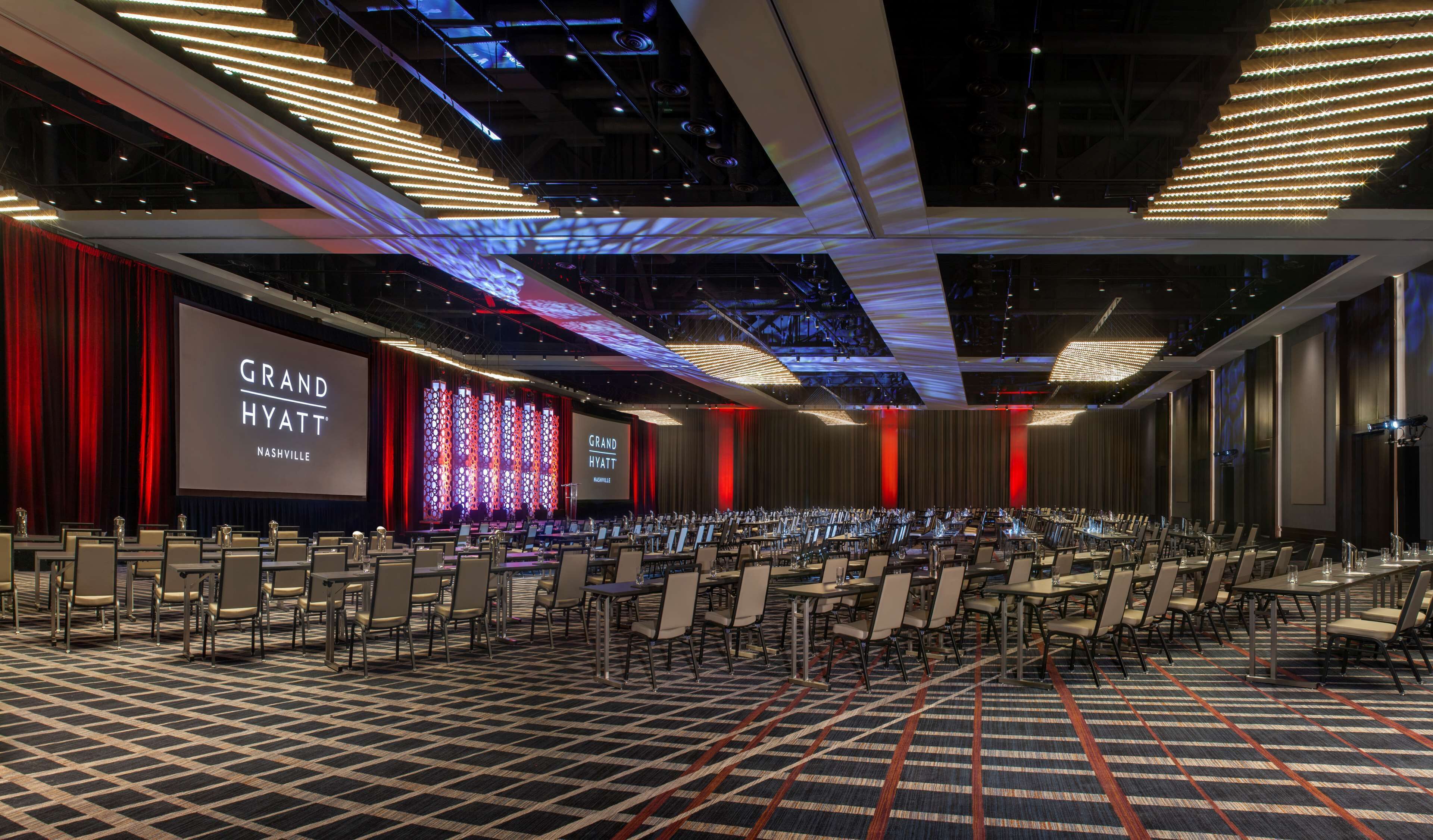 Una sala de conferencias en el Grand Hyatt Nashville con un escenario, filas de sillas y una alfombra estampada.