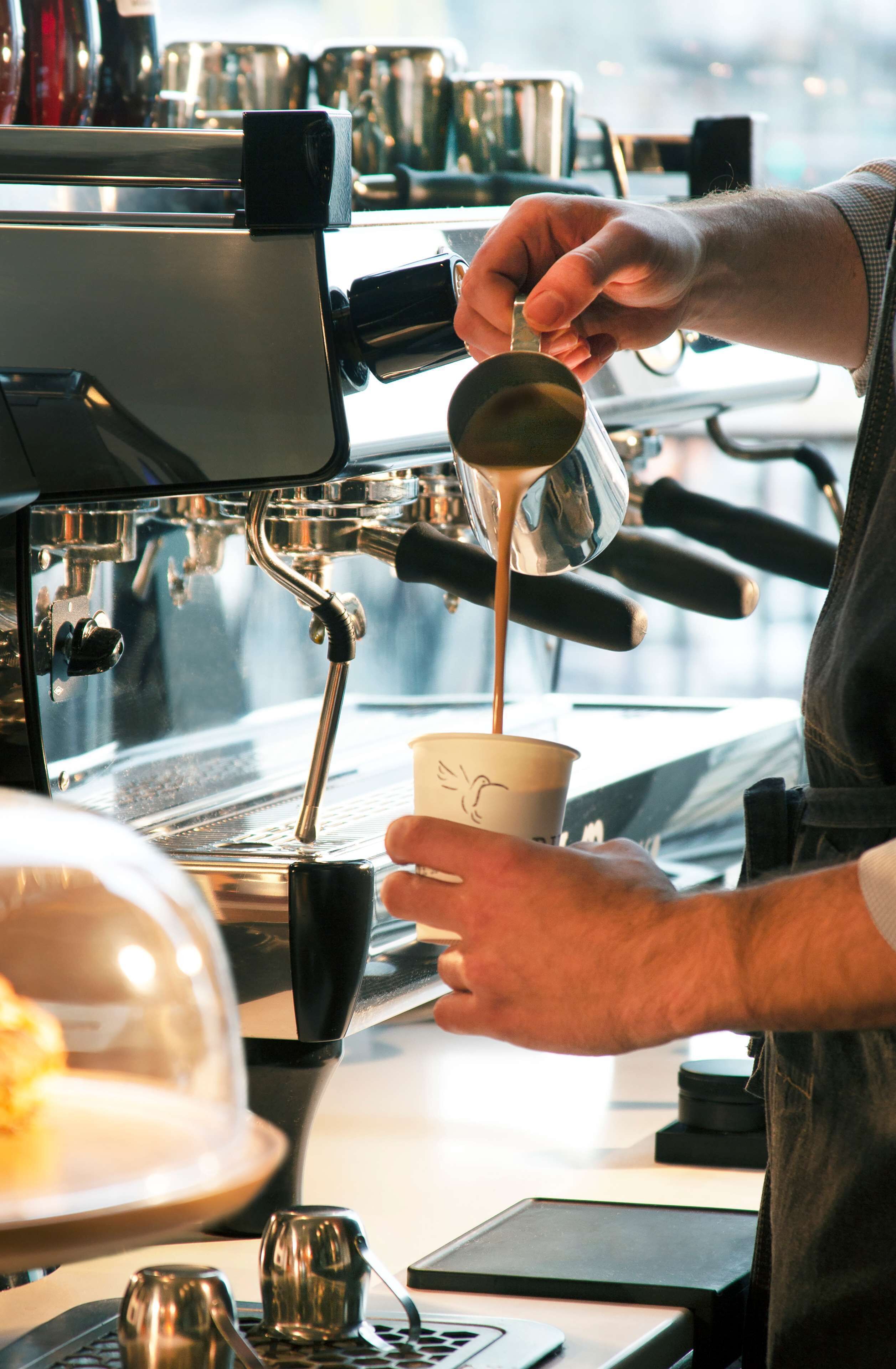 A person pouring coffee into a cup at a coffee machine.