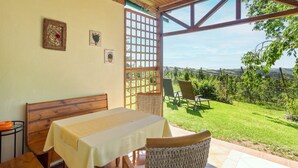 Un patio cubierto con una mesa y sillas, un banco de madera y vistas a un paisaje verde a través de una ventana celosía.