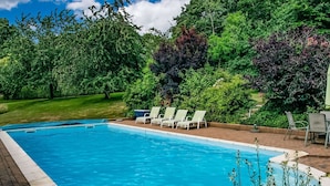 Une piscine rectangulaire bordée de blanc, entourée d’une terrasse en briques. Plusieurs chaises longues blanches sont alignées le long du bord de la piscine.