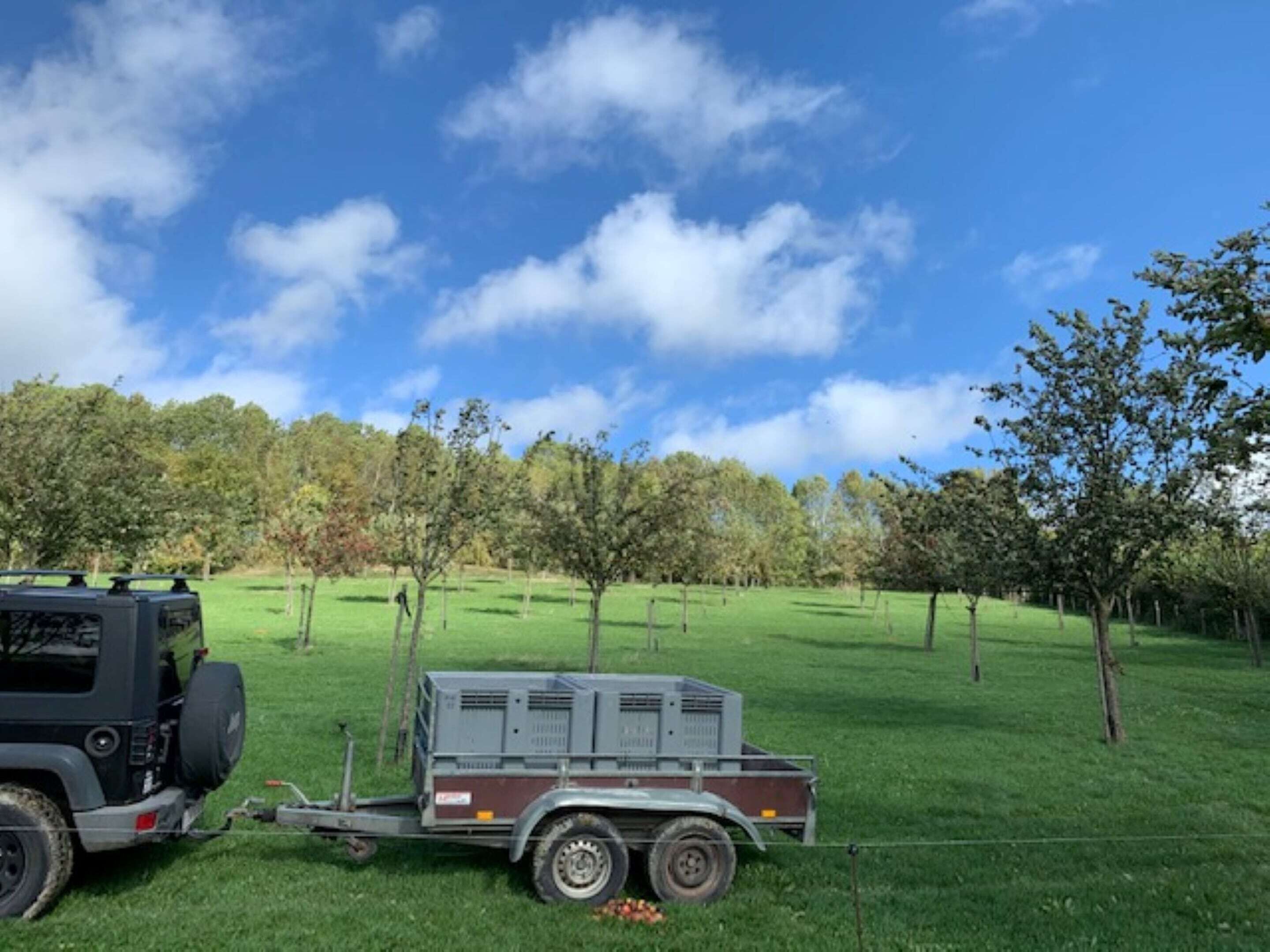 A trailer with a generator and a black vehicle parked in a grassy field with trees in the background.