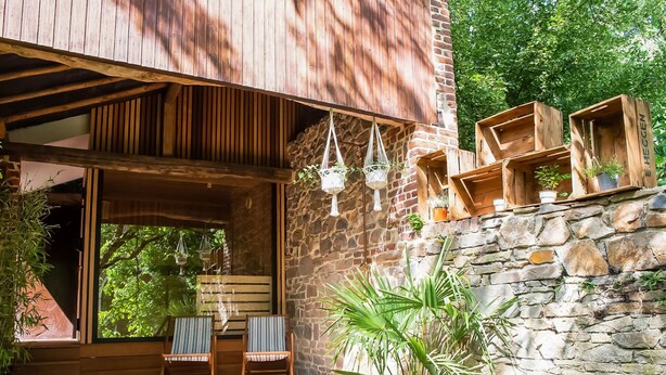 Une terrasse en bois avec deux chaises à rayures, un mur en pierre et des jardinières suspendues.