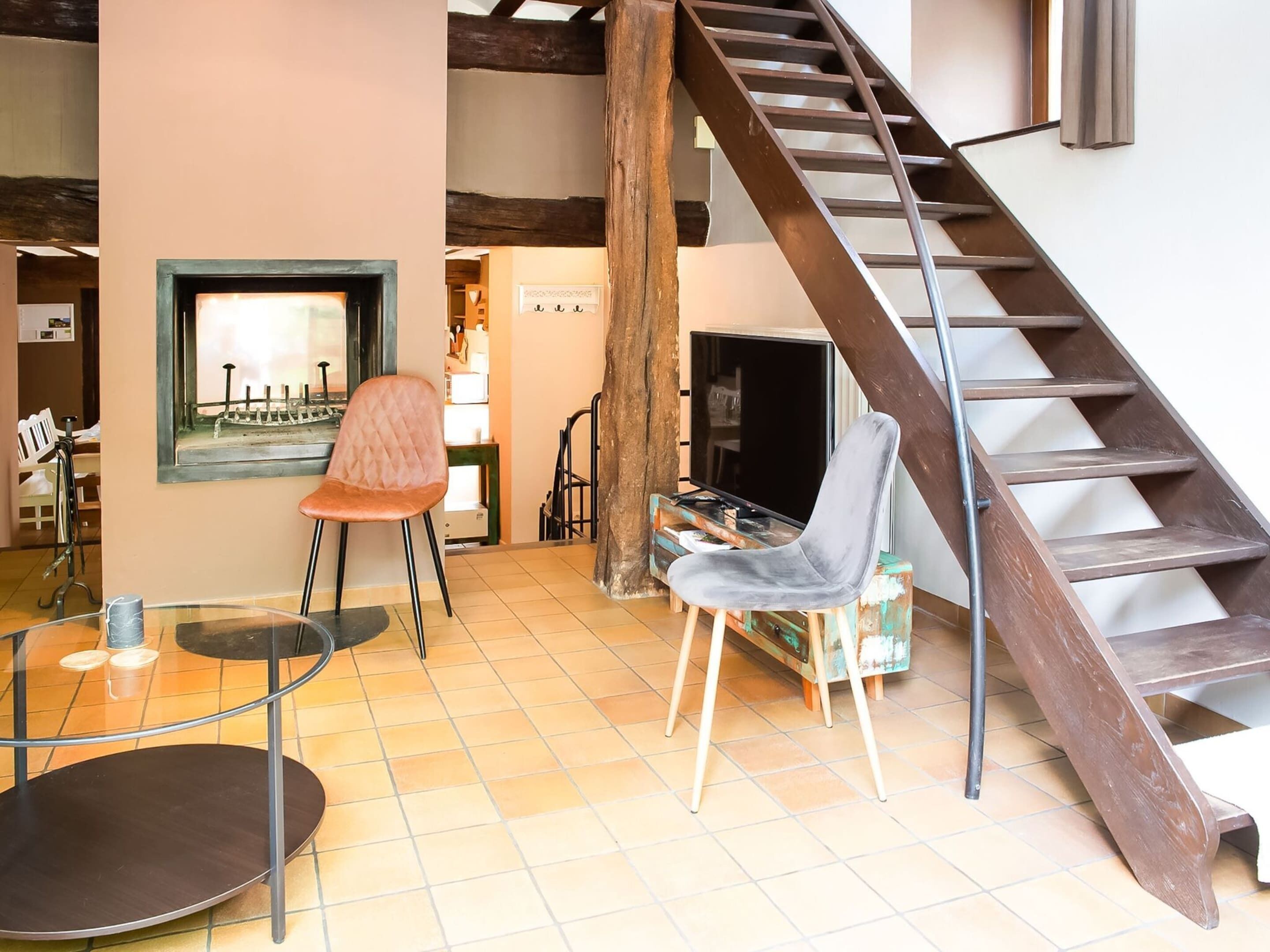 A spacious living area with a wooden staircase, a television, and two chairs.
