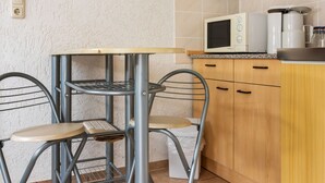 A compact kitchen with a small table and two chairs, a microwave, and wooden cabinets. - Ferienhaus in Meisdorf (Falkenstein)
