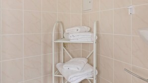 A bathroom with beige tiled walls, a white towel rack with folded towels, and a visible electrical outlet. - Ferienhaus in Meisdorf (Falkenstein)