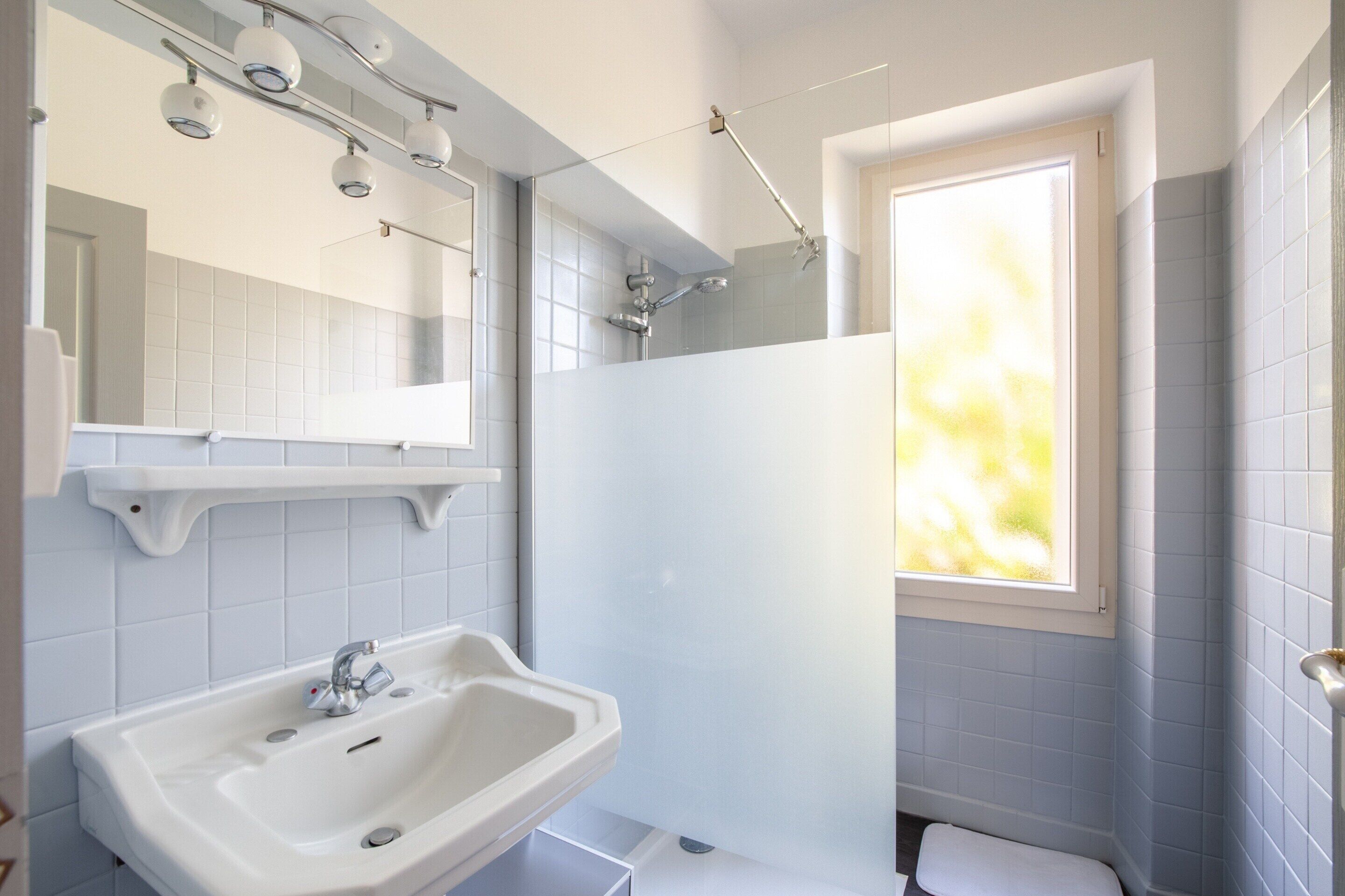 Une salle de bain avec un lavabo, un miroir, une douche et une fenêtre.