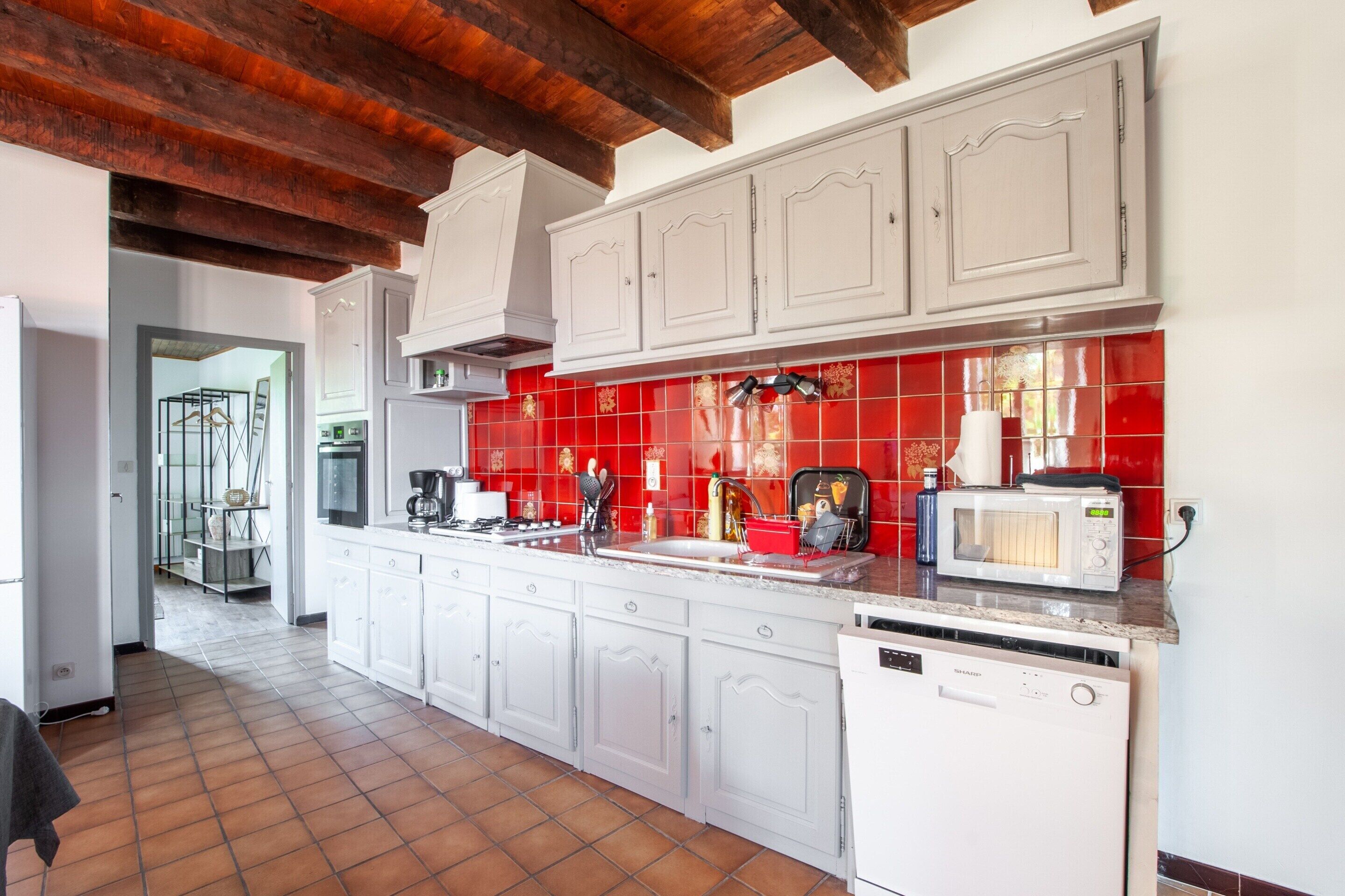 A kitchen with white cabinets, a red backsplash, and a dishwasher.