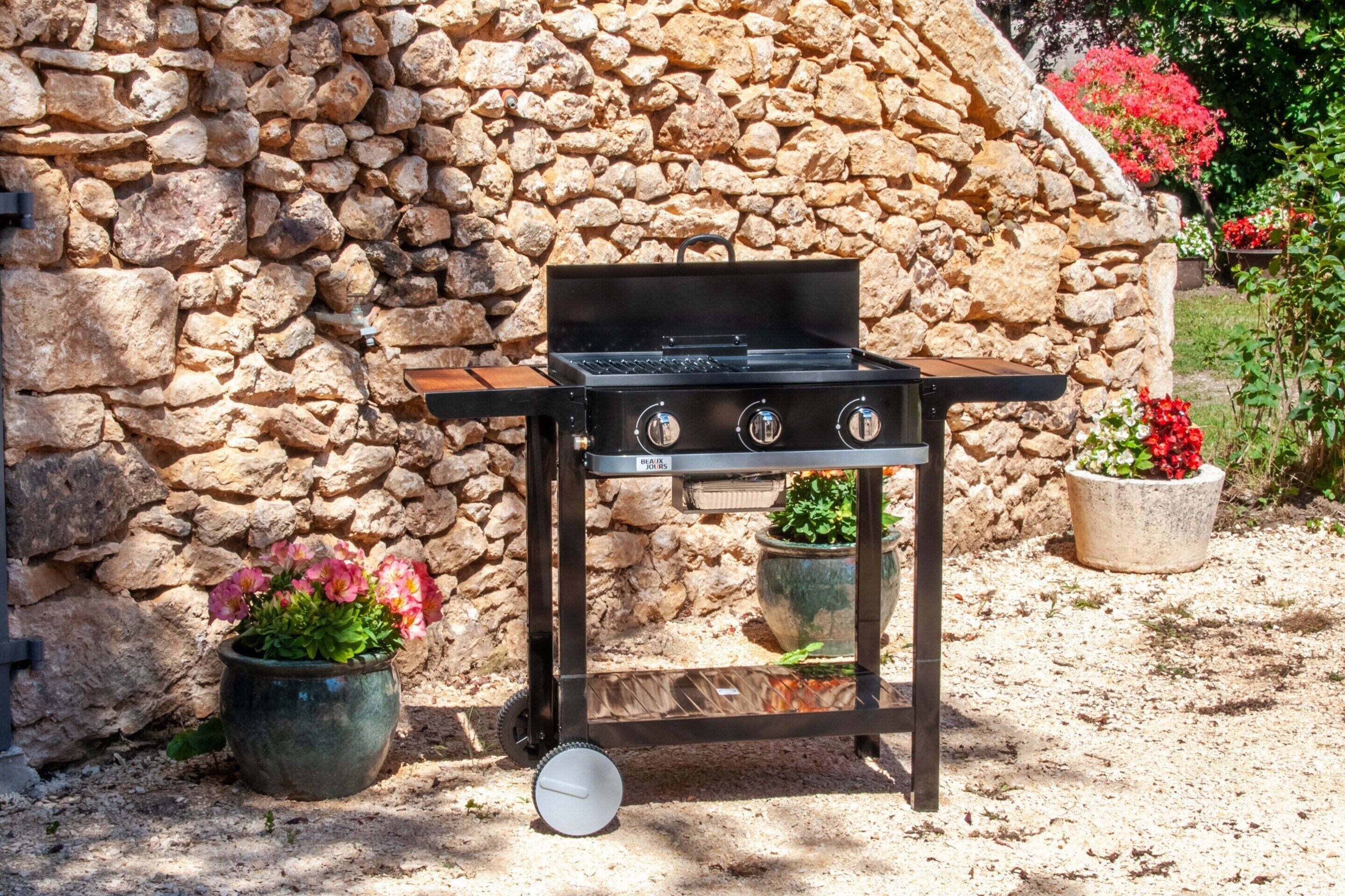 A portable grill with a stone wall backdrop, potted plants, and a clear view of the surrounding garden.