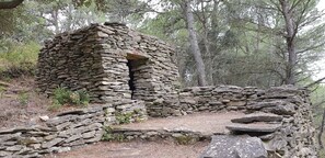 A stone structure with a doorway, surrounded by trees and a forested area. - Modern Villa in Camplong With Private Pool (Felines-Minervois)